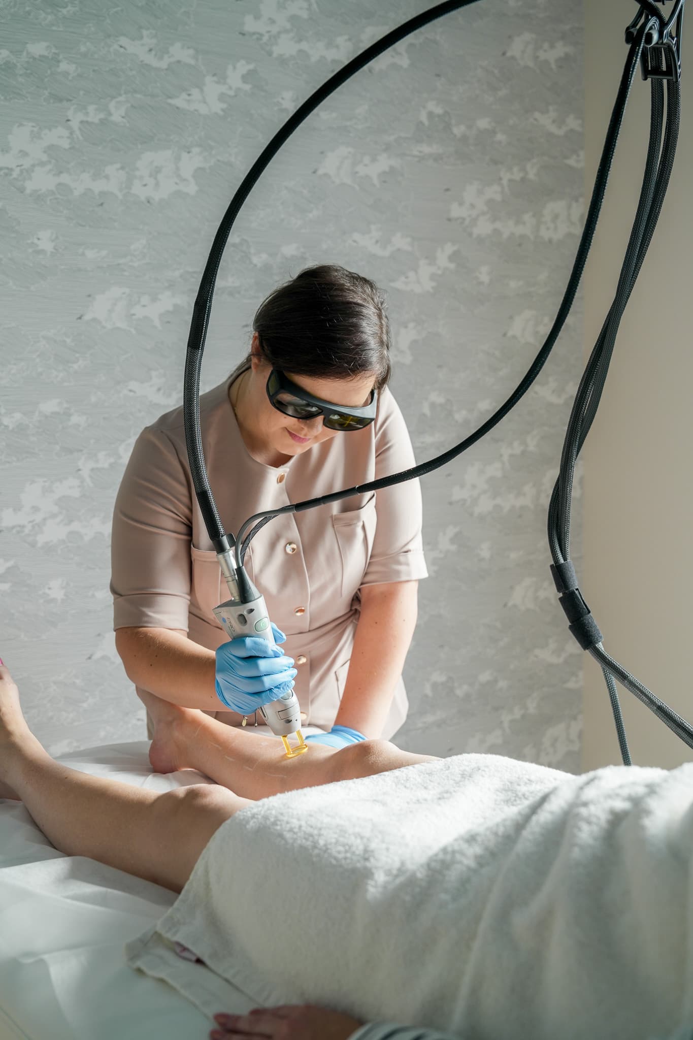Specjalistka Lumelle w okularach ochronnych podczas zabiegu laserowego na nodze pacjentki