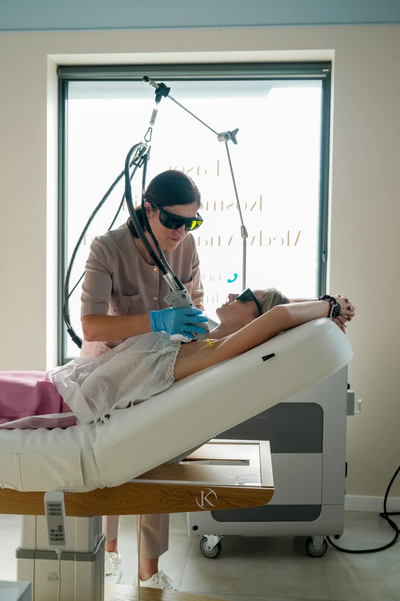 Specjalistka Lumelle prowadzi głowicę lasera Candela w okolicy pachy klientki w okularach ochronnych, za łóżkiem urządzenie
