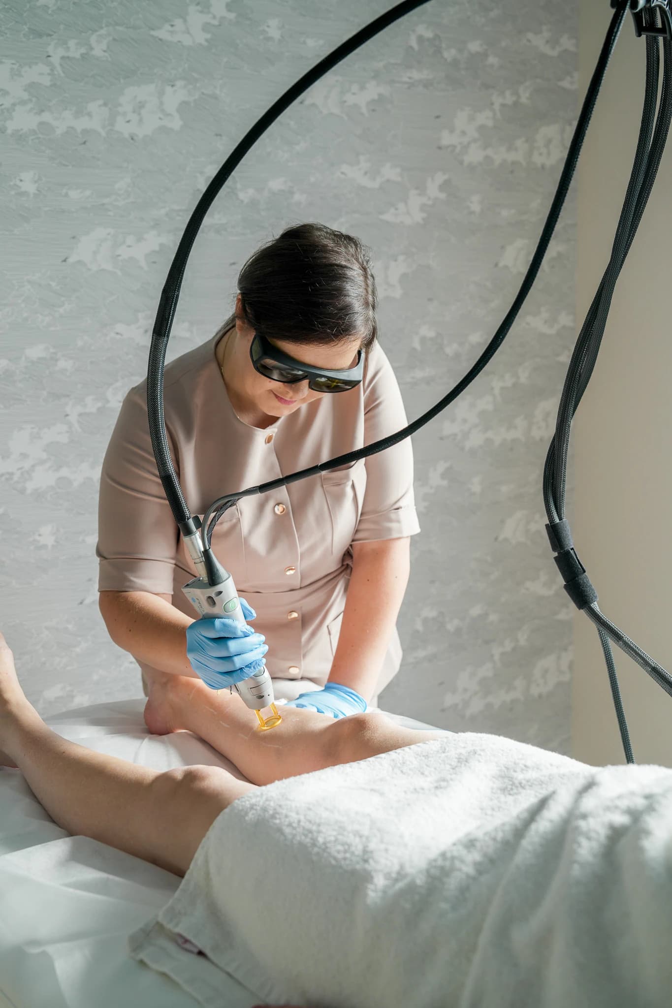 Depilacja laserowa Candela - specjalistka w okularach ochronnych prowadzi głowicę lasera po nodze klientki